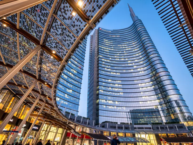 A glass tower in Milan rises above a curved, textured glass canopy.