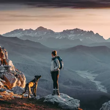 Woman hiking and looking at the view on the top of a mountain with a beautiful landscape at sunrise.
1316421598