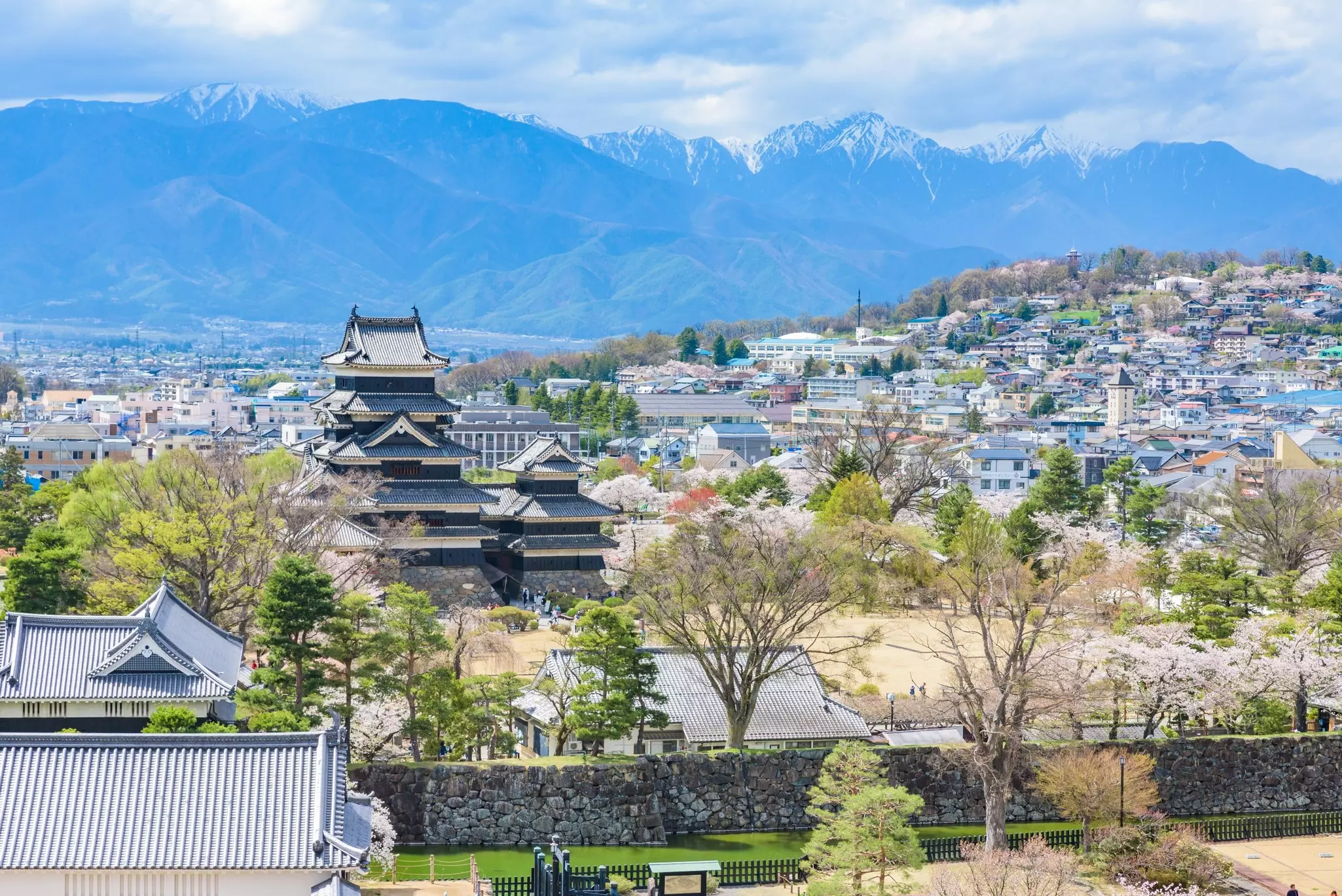 Trees in blossom and mountain ridges frame Matsumoto-jo castle in spring, Matsumoto, Nagano Prefecture. Japan.