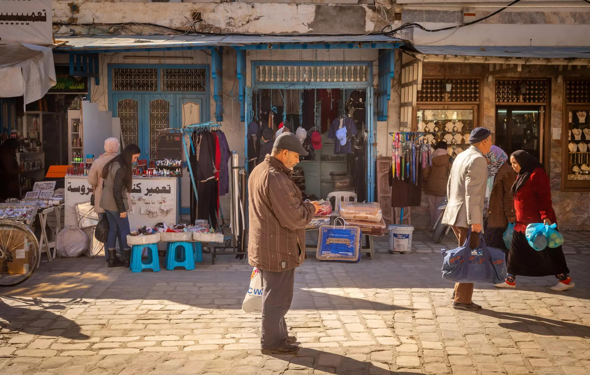 An elderly Tunisian man stops to look at his mobile phone in a busy souk
