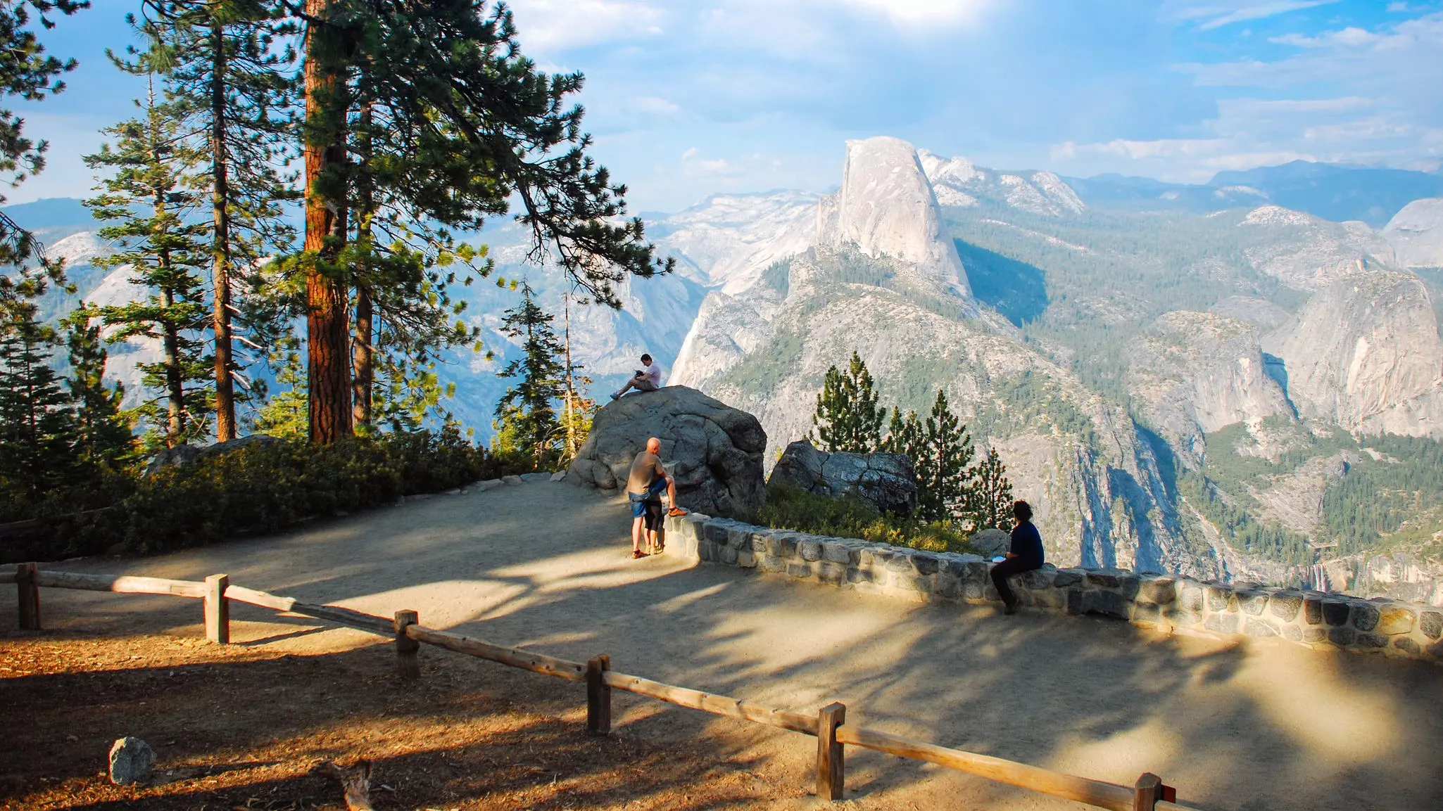 Two people look at a mountain in the distance from an overlook with a stone wall boundary