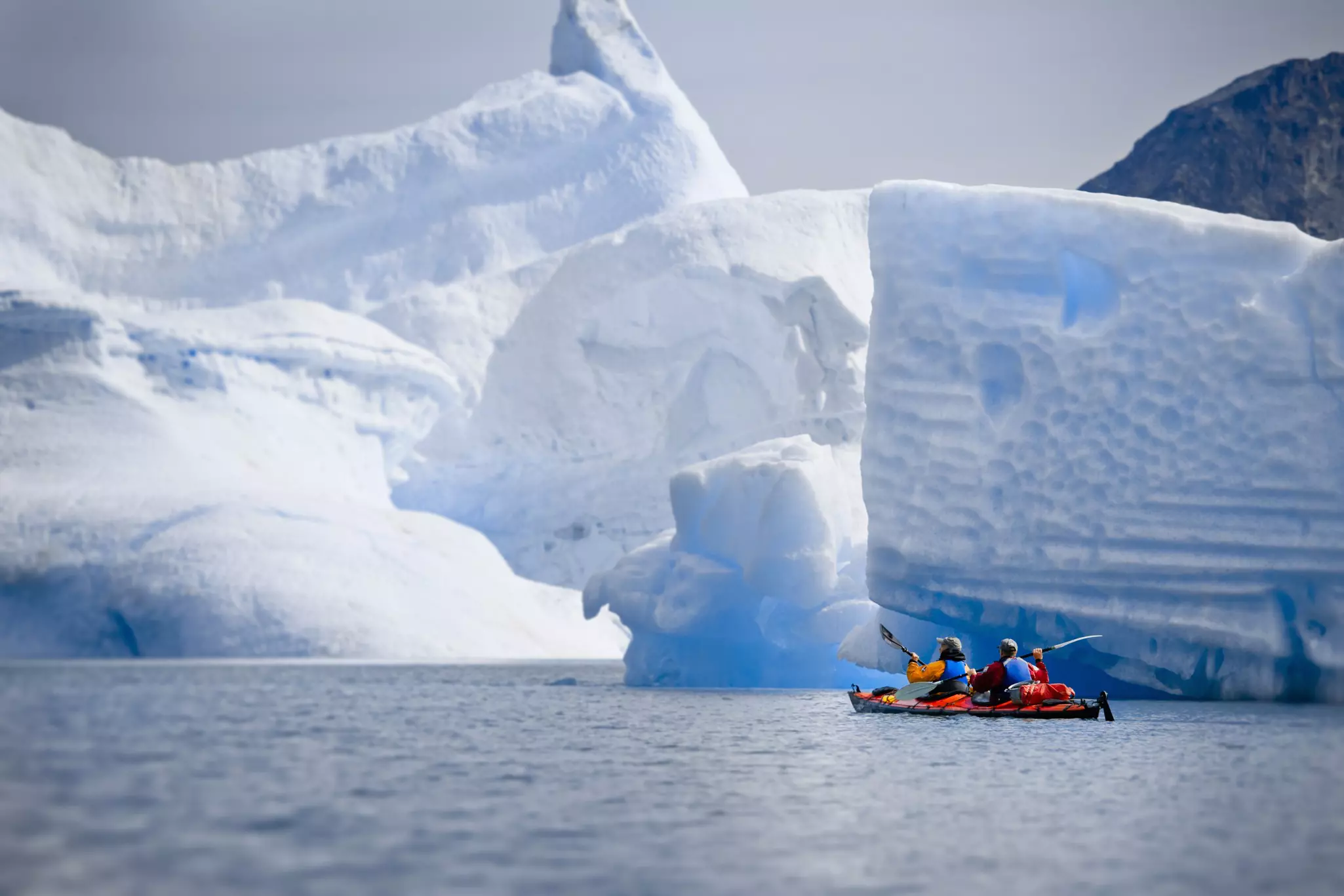 Two people in a tandem kayak paddle toward glaciers.