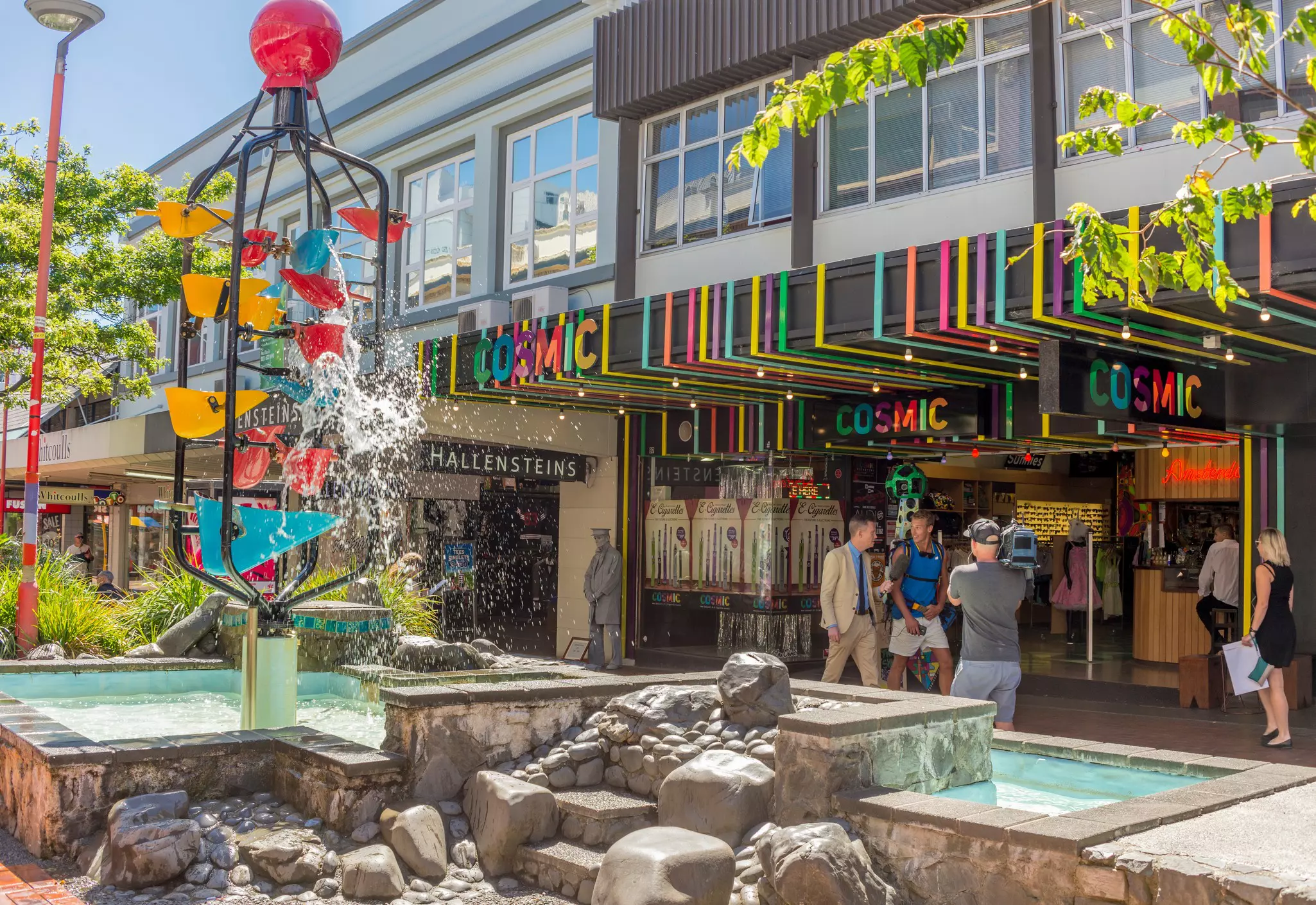 A pedestrianized shopping street with a large installation of a series of buckets spilling water.