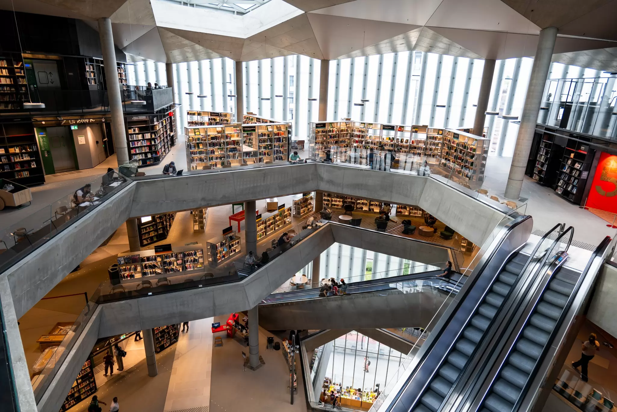 Escalators pass through a multi-floored space flooded with light. People work and play within: Deichman Bjørvijka, Oslo library