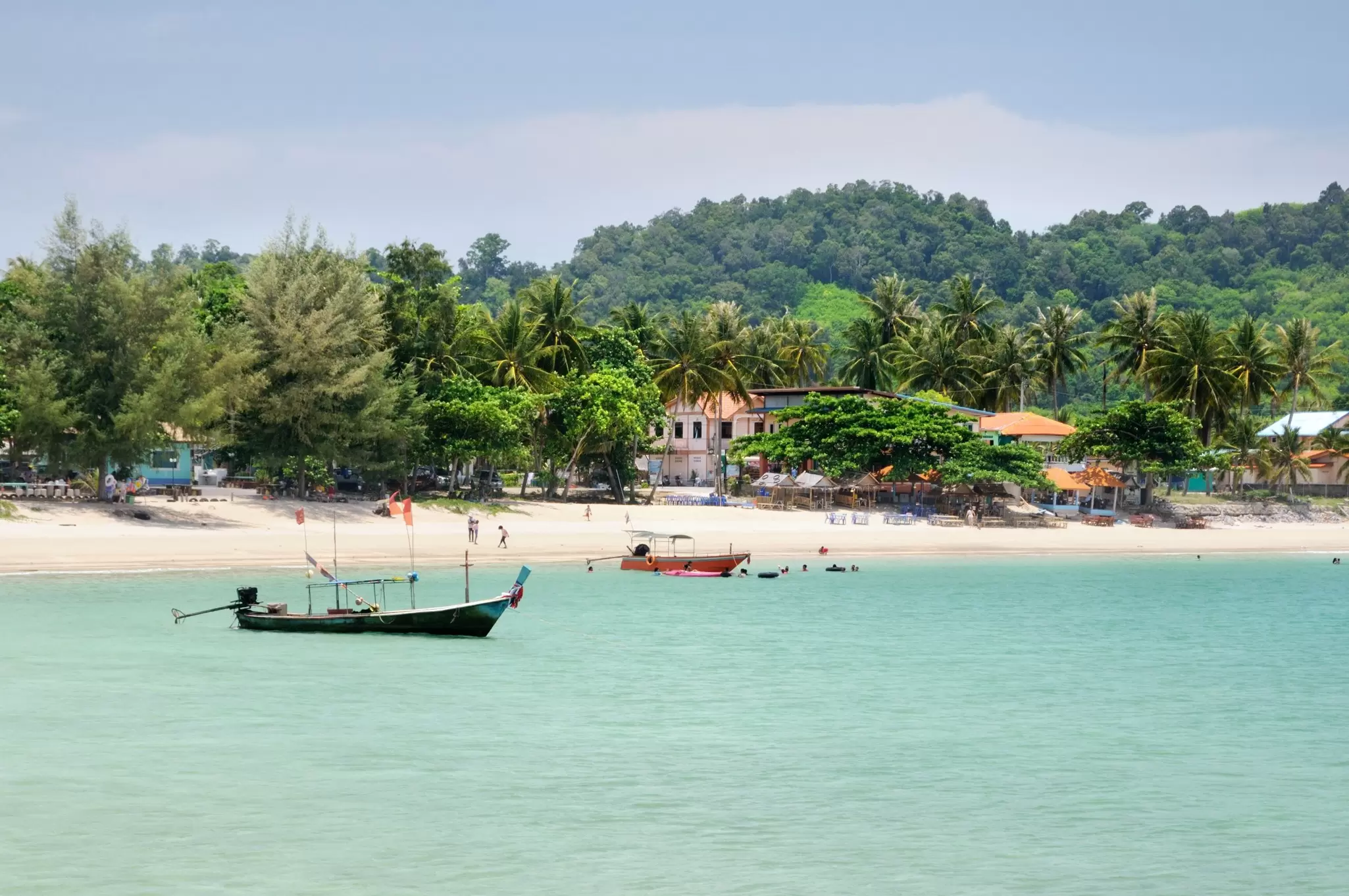 A palm tree-lined beach with several colorful fishing boats moored near the shore.