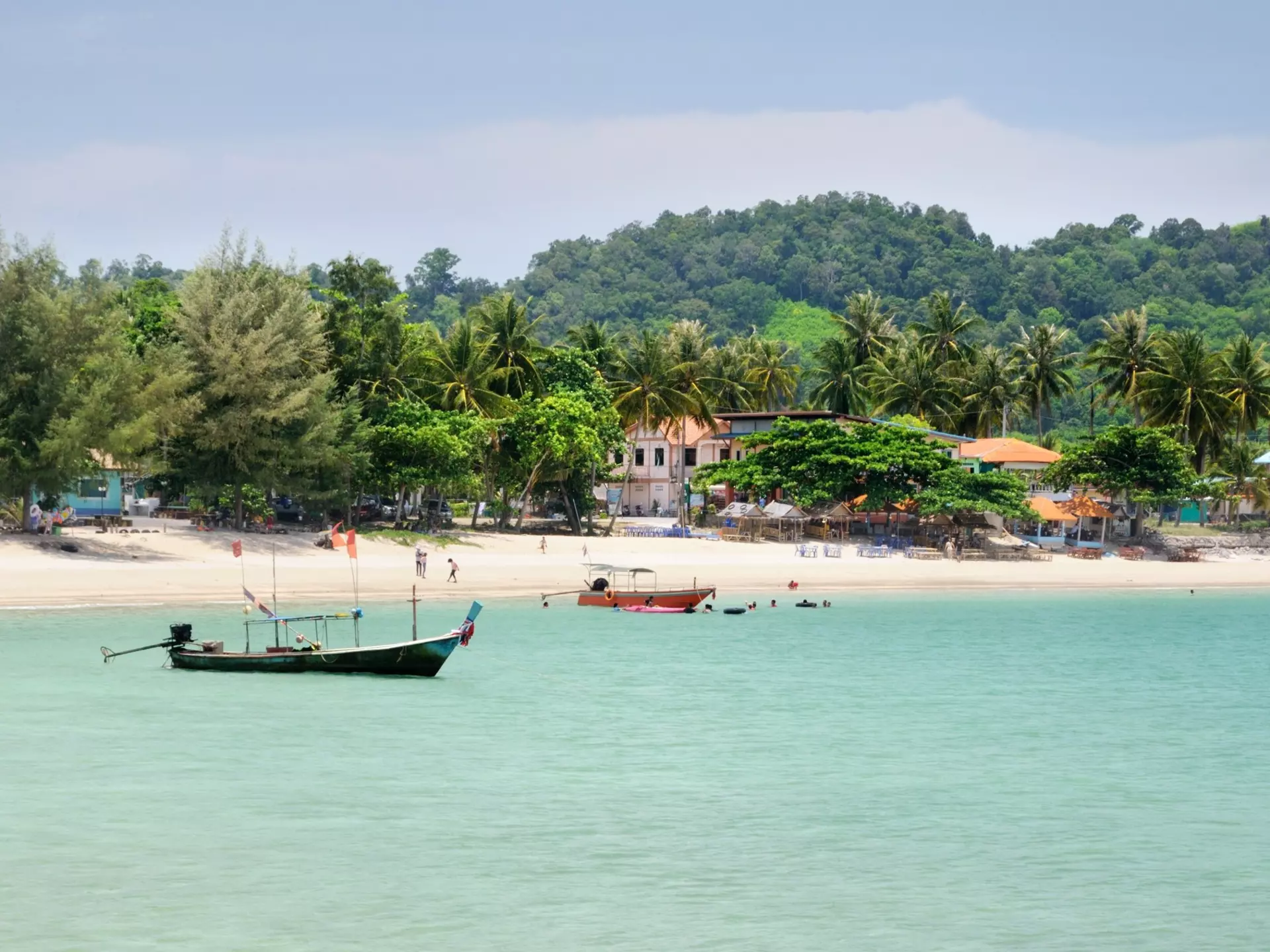A palm tree-lined beach with several colorful fishing boats moored near the shore.