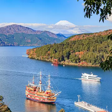 Replica sailing ship and cruise boat on Lake Ashi, Hakone, with a red torii on the wooded shore and snowy Mt Fuji behind