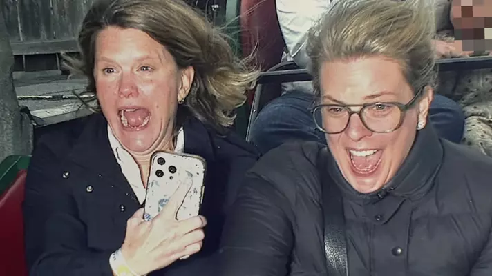 Close-up of two women happily screaming while riding a rollercoaster.