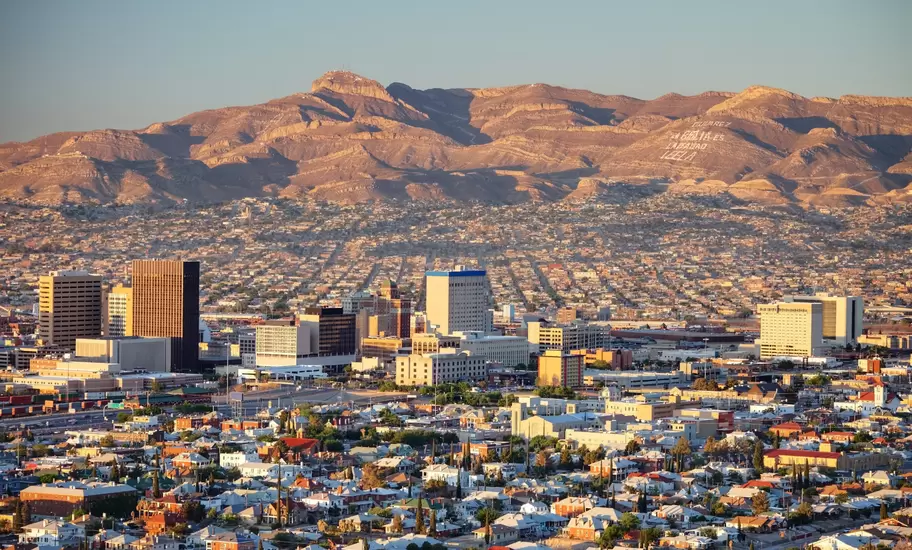 Downtown El Paso, Texas, at golden hour; behind, Juárez mountains bear the words 'Cd Juarez La Biblia es la verdad Leela'