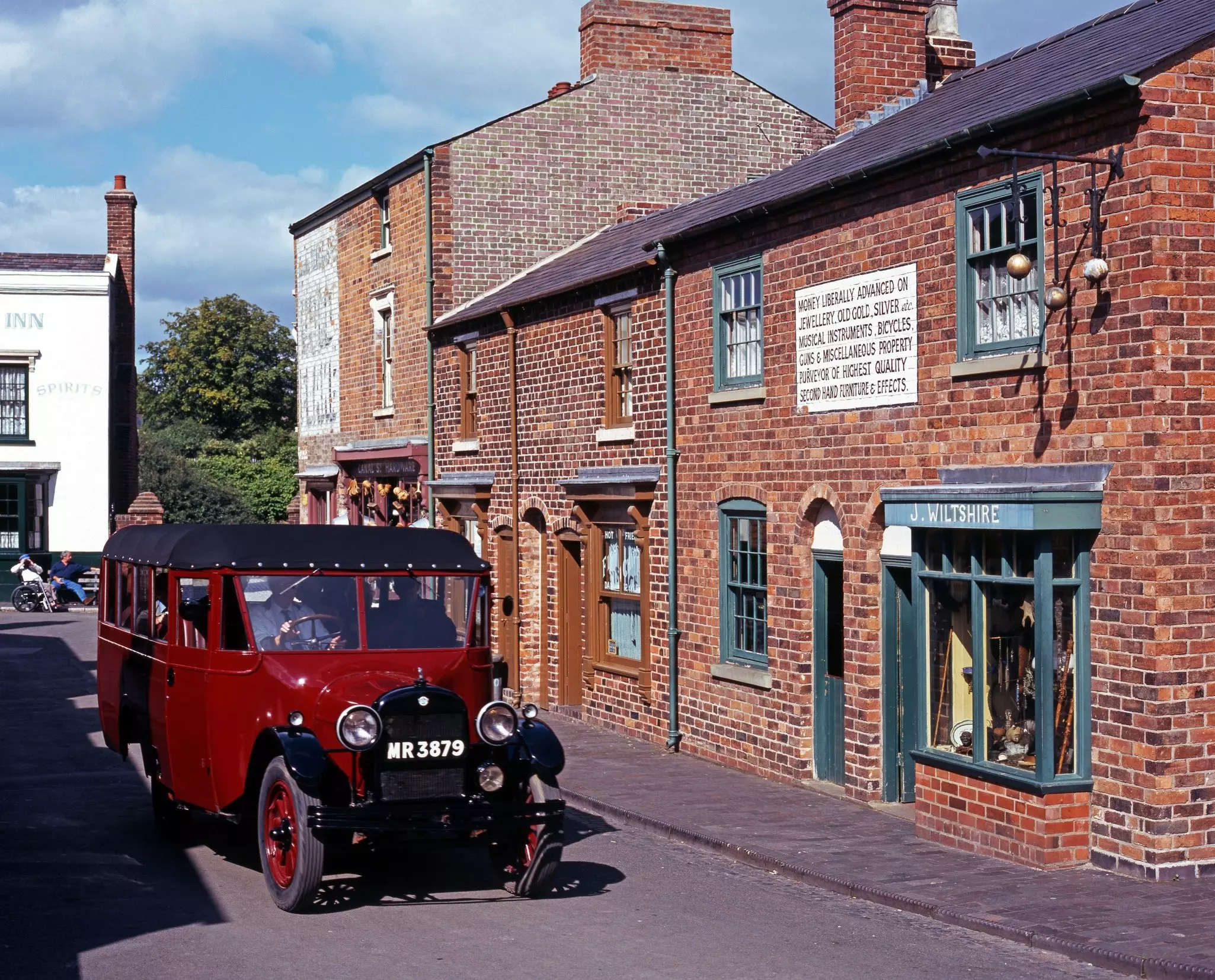 A red vintage car drives past the redbrick buildings of a Victorian main street at an open-air museum in England.