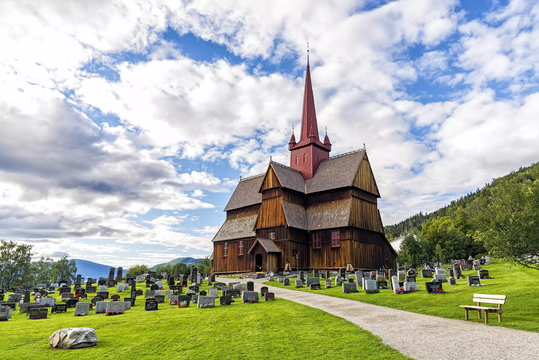 A path runs to a wooden stave church that sits at the top of a grassy lawn with gravestones.