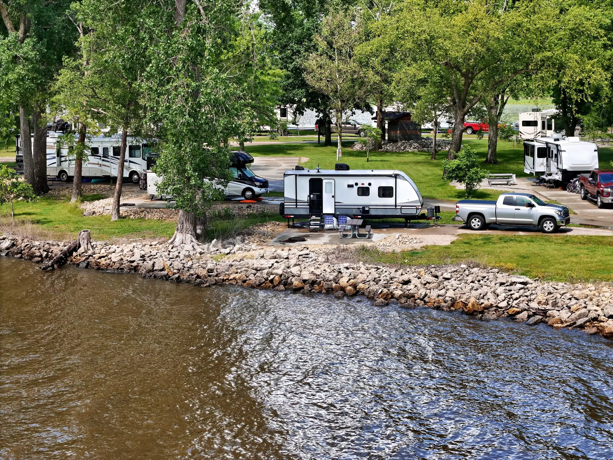 Trailers and RVs shaded by trees along the Mississippi River in Illinois