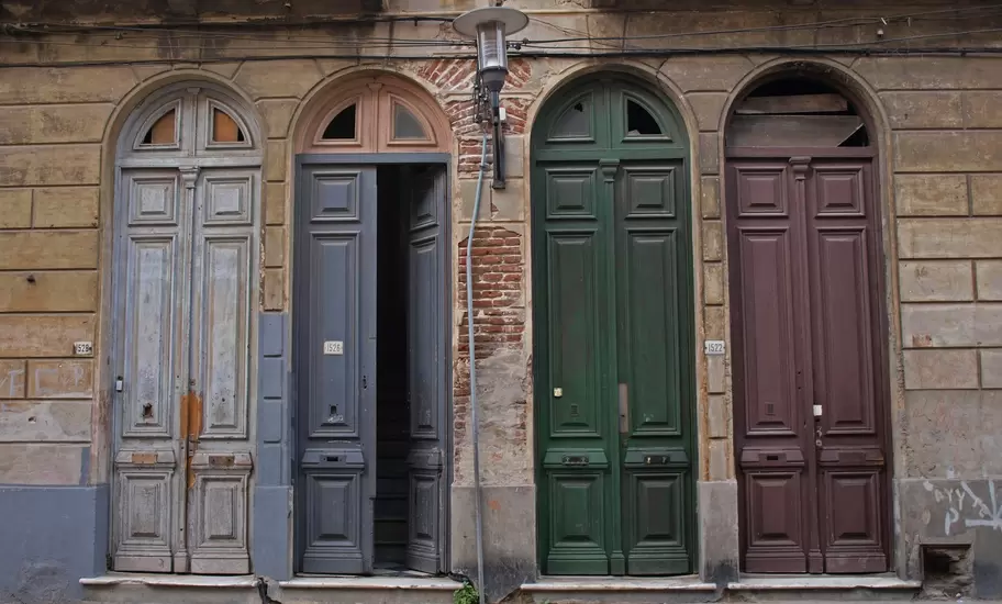 Four tall arched wooden doors in grey, green and maroon on a weathered stone facade in Montevideo's old town, Uruguay