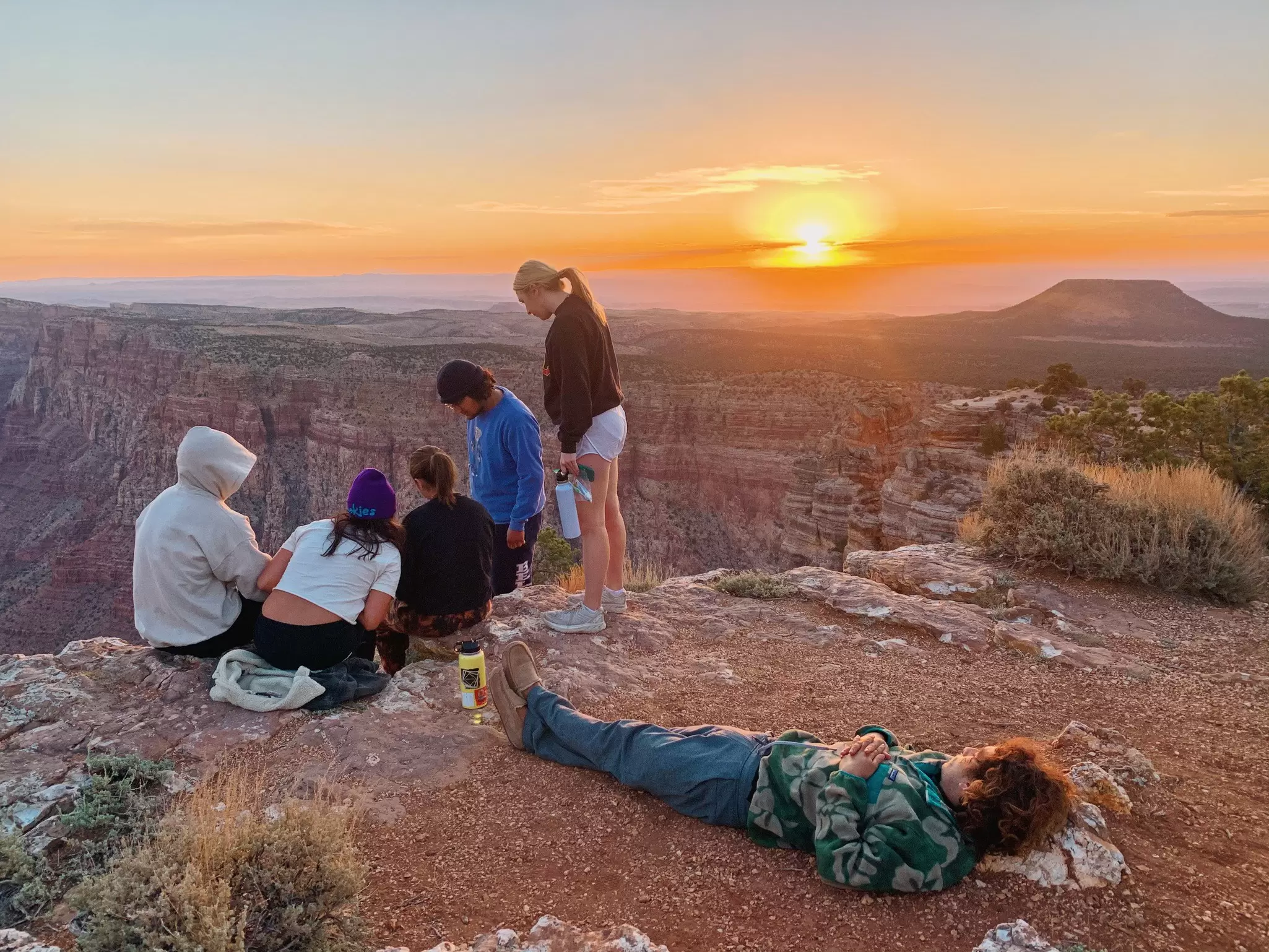 A small group of people at a viewpoint above a canyon as the sunrise fills the sky