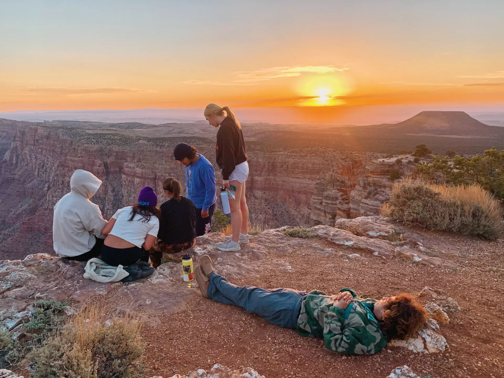 A small group of people at a viewpoint above a canyon as the sunrise fills the sky