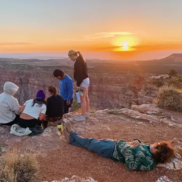 A small group of people at a viewpoint above a canyon as the sunrise fills the sky