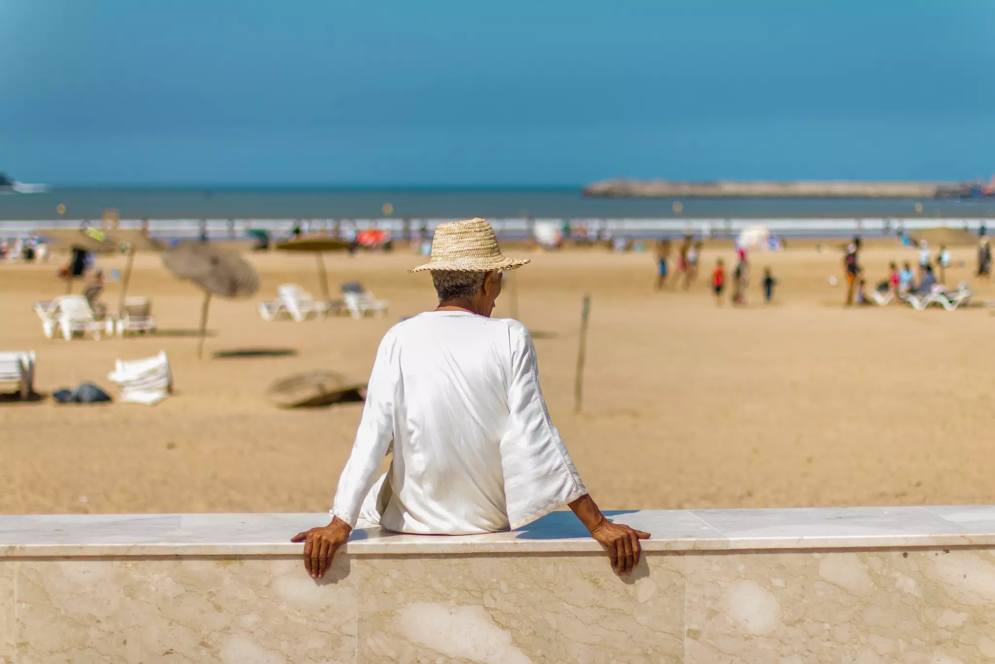 Man in a white tunic and a straw hat sitting on the beach in Essaouira, Morocco, Africa