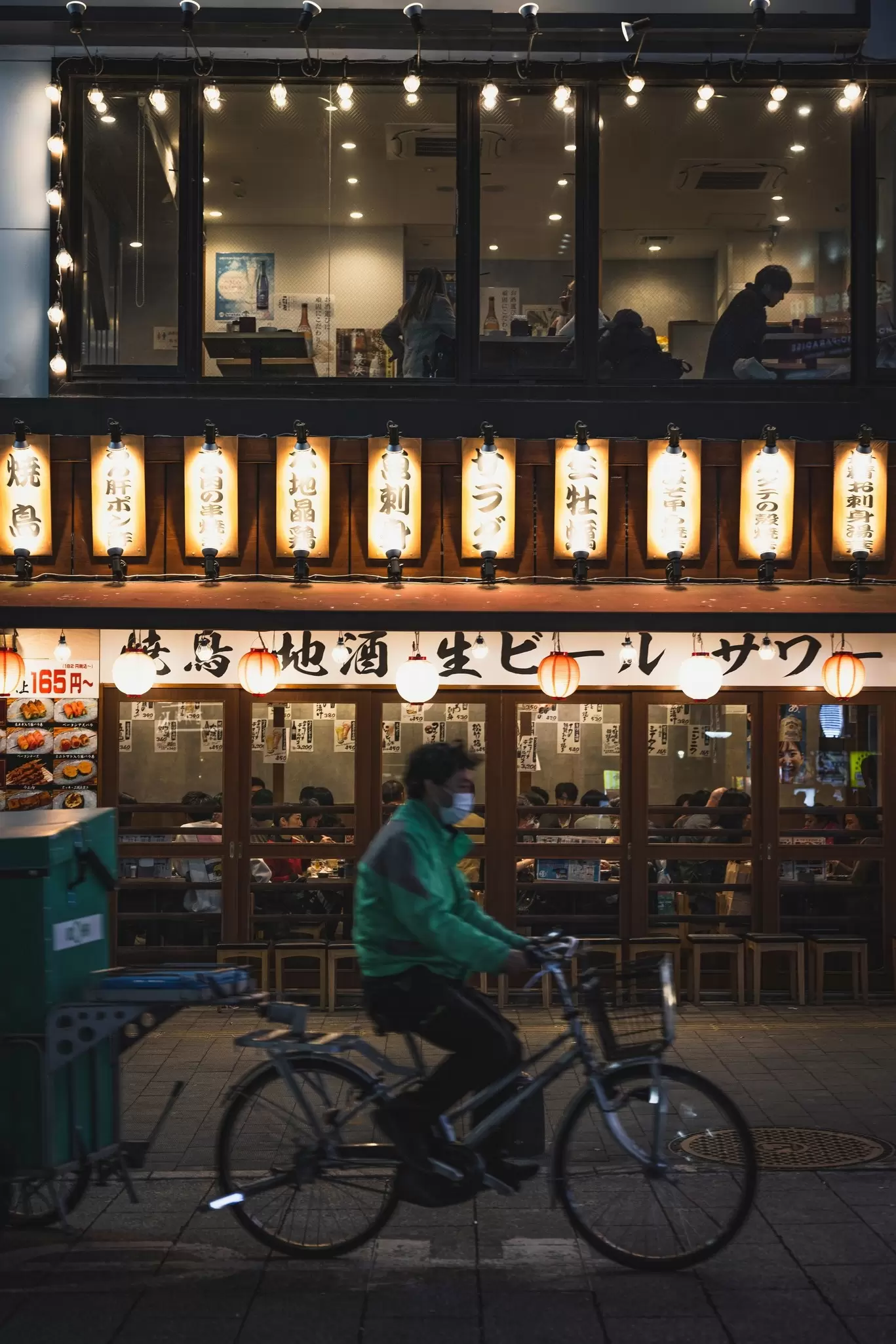A person on a bike cycles past a brightly lit building in Shibuya