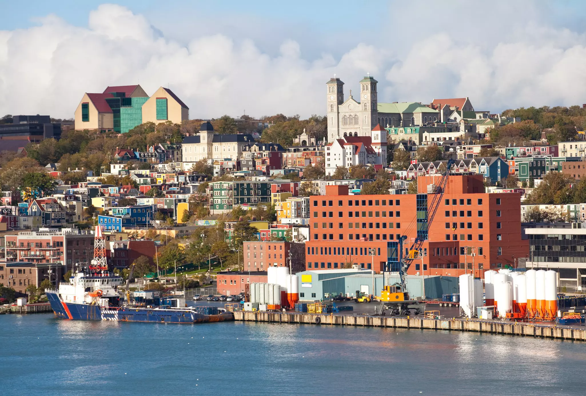 A mix of city buildings and colorful homes with a harbor in the foreground on a mostly sunny day.