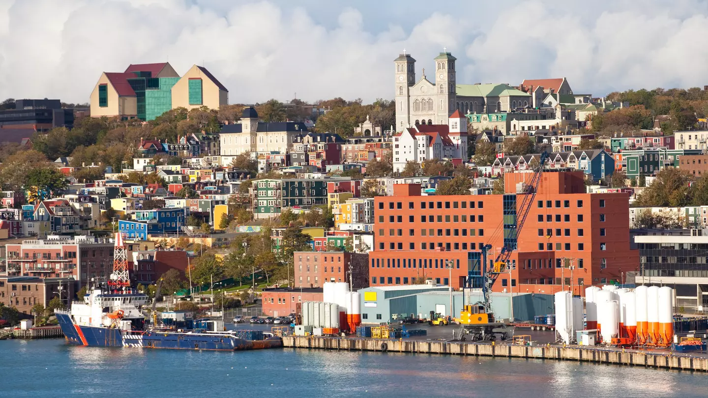 A mix of city buildings and colorful homes with a harbor in the foreground on a mostly sunny day.