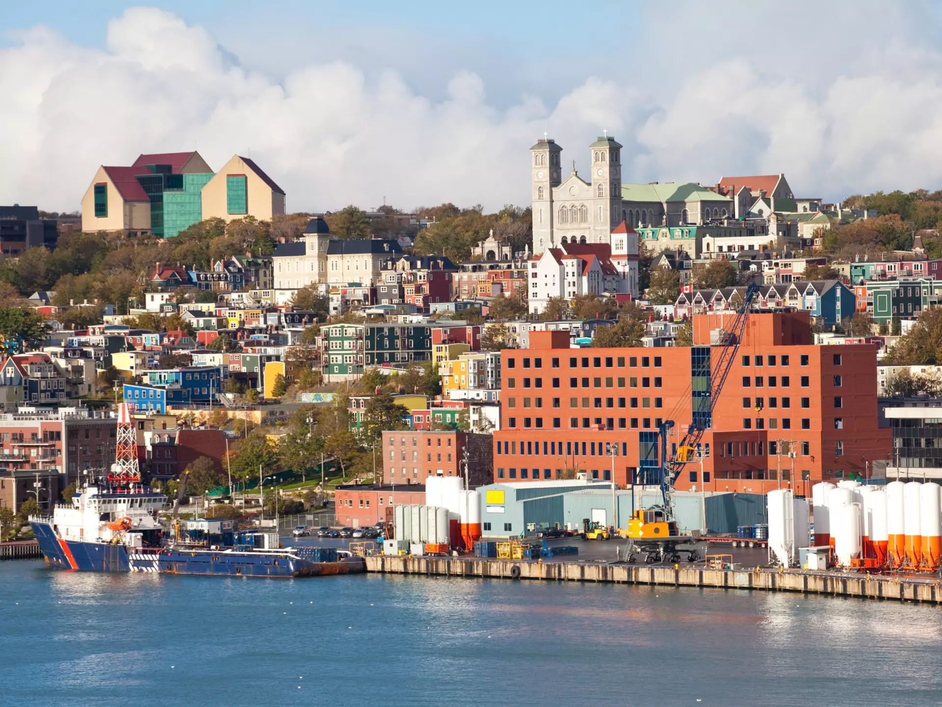 A mix of city buildings and colorful homes with a harbor in the foreground on a mostly sunny day.