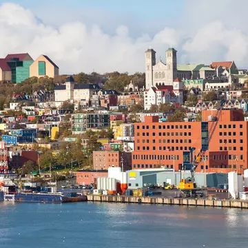 A mix of city buildings and colorful homes with a harbor in the foreground on a mostly sunny day.