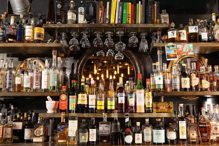 Shelves contain dozens of bottles of liquor behind a bar at a cocktail lounge.