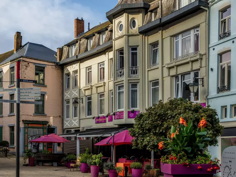 Traditional historic buildings featuring classical Belgian architecture with colorful flowers and small trees planted in front