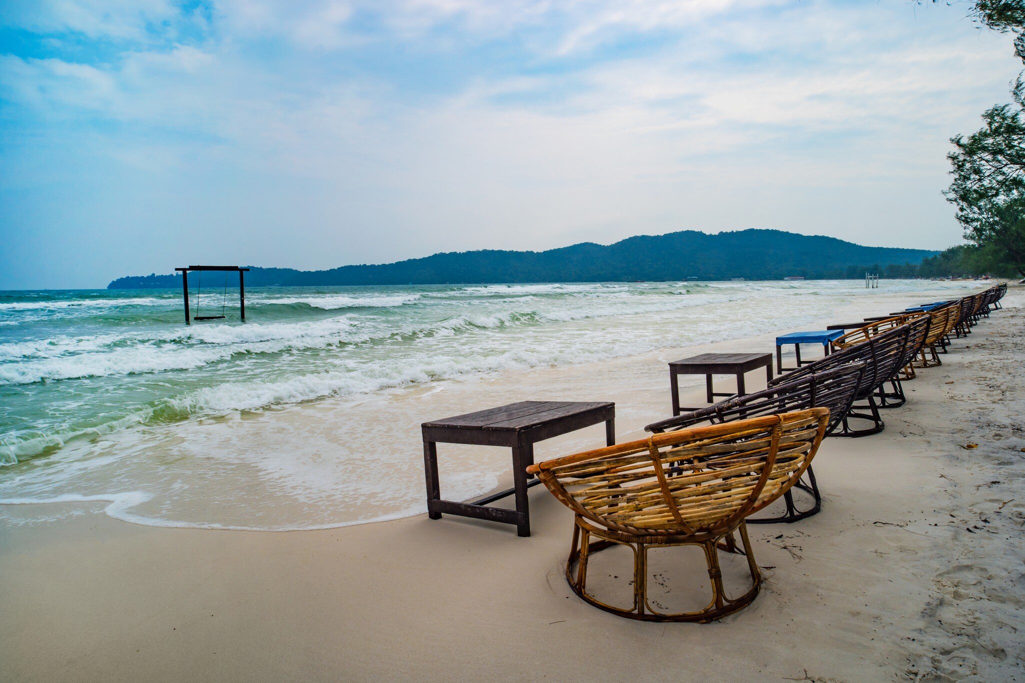 Wooden cafe table and chairs on a tropical beach with blue sea on background. island Koh Rong Samloem, Saracen Bay. Cambodia.