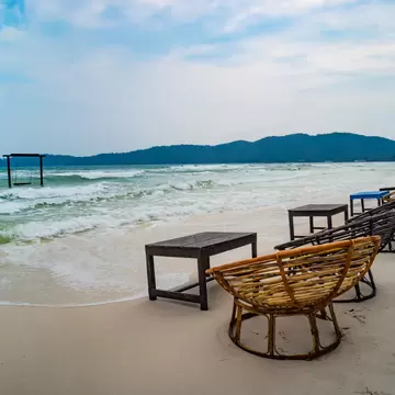 Wooden cafe table and chairs on a tropical beach with blue sea on background. island Koh Rong Samloem, Saracen Bay. Cambodia.