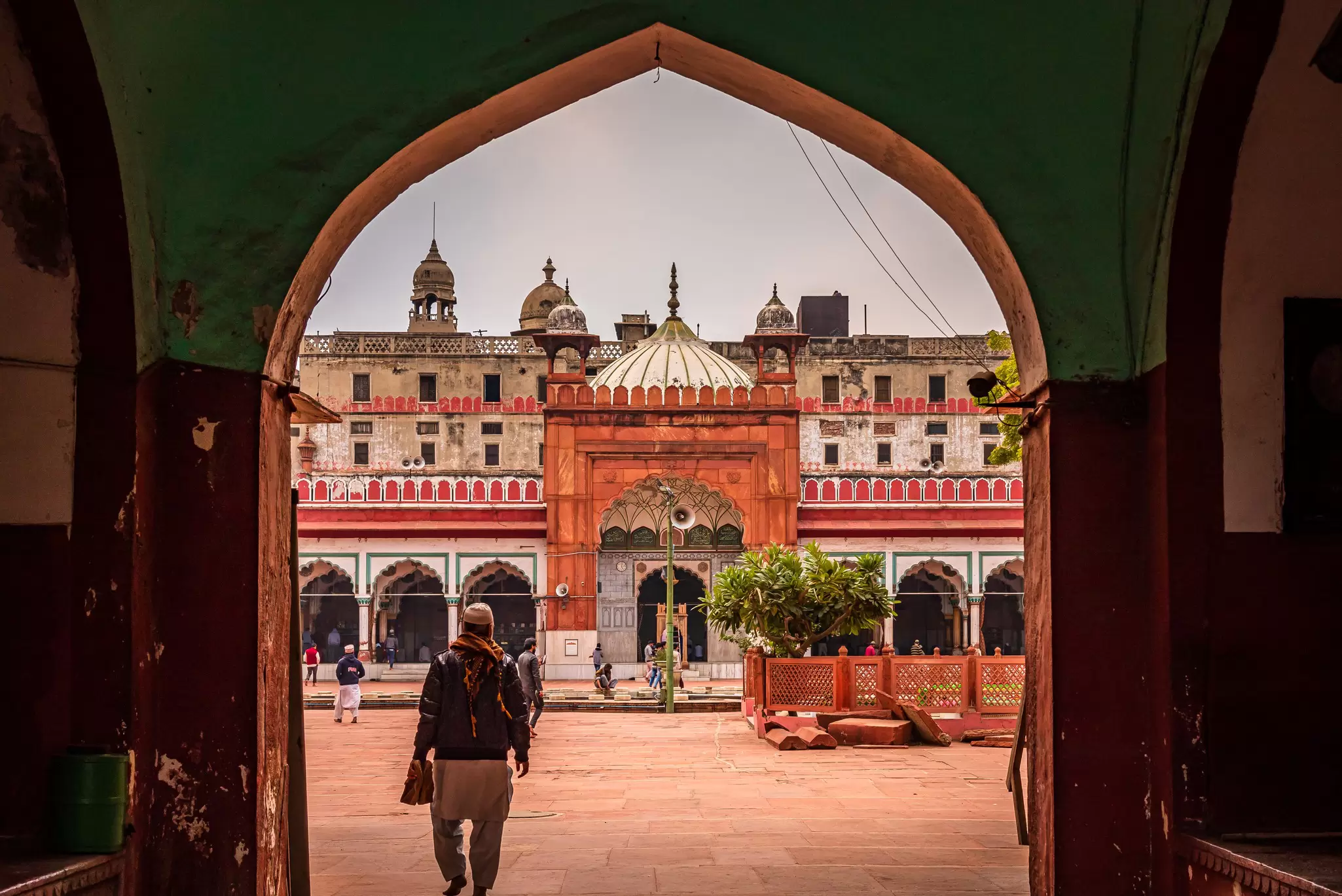 A person walks through an archway toward a courtyard in front of a mosque.