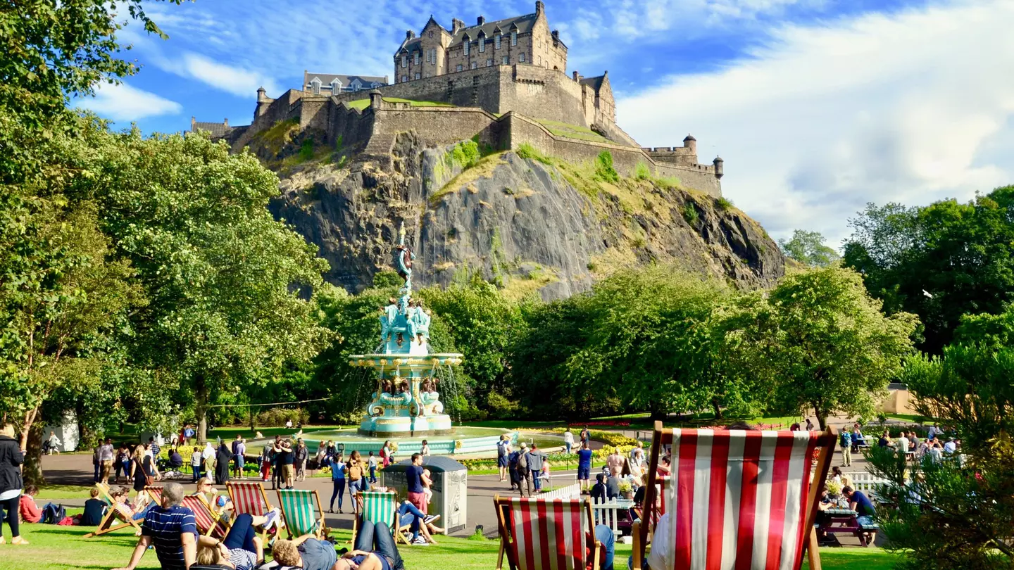 People relaxing near Ross Fountain in Princes Street Gardens on a sunny day, with Edinburgh Castle above