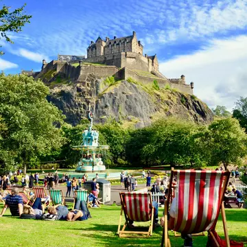 People relaxing near Ross Fountain in Princes Street Gardens, with Edinburgh Castle above.