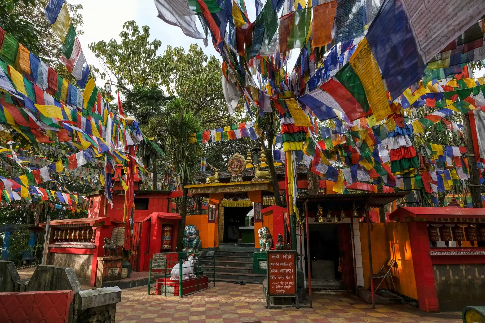 Prayer flags are overhead in a courtyard in front of a temple with a decorated gate.