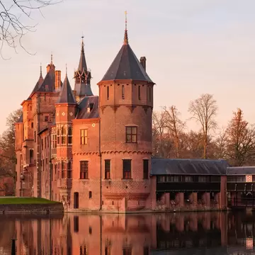 View of the setting sun shining on Kasteel de Haar near Utrecht, as seen from across a pond.