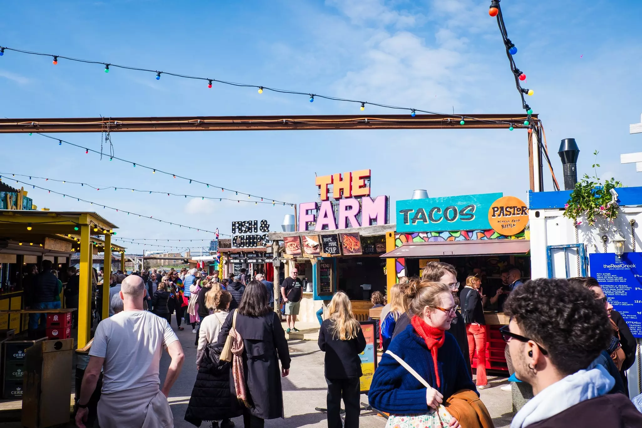 A byusy street-food market with people wandering around among wooden cabins and stalls serving food.