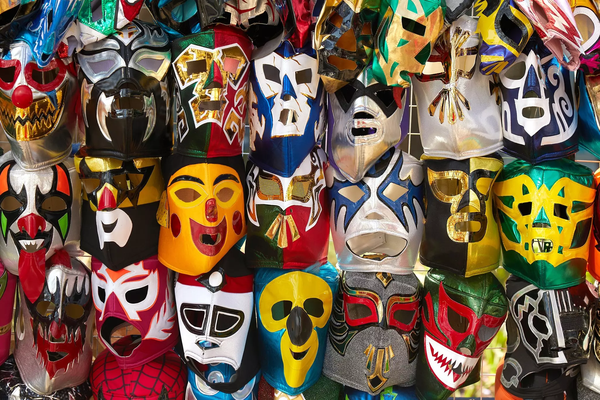Many colorful leather wrestling masks hanging on a display