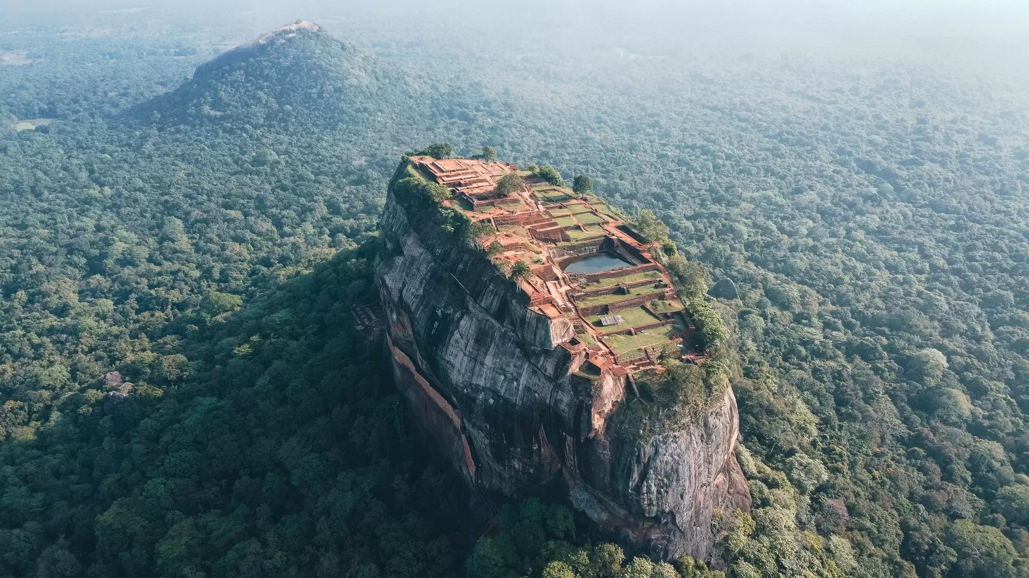 Aerial view of ancient ruins on top of a huge rock surrounded by dense forest.