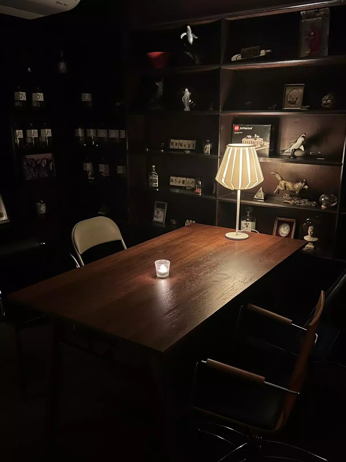 A dim room with dark furniture and a table lamp and a small candle lighting the room
