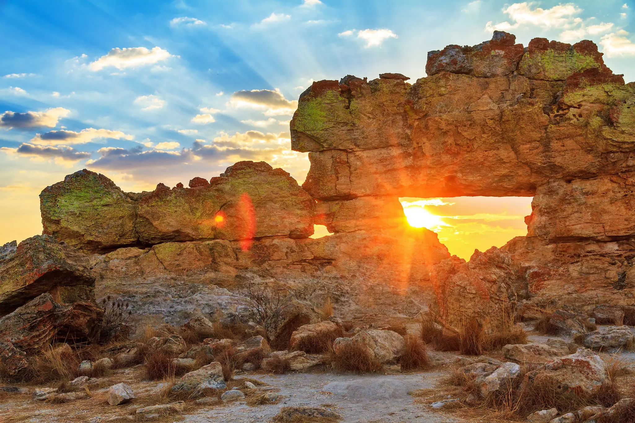 The setting sun is framed within the opening of a rugged rock formation