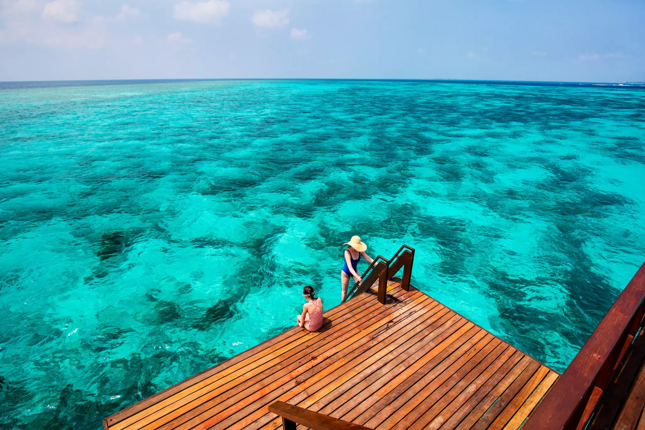 Mother and daughter at wooden dock of overwater villa in Maldives.