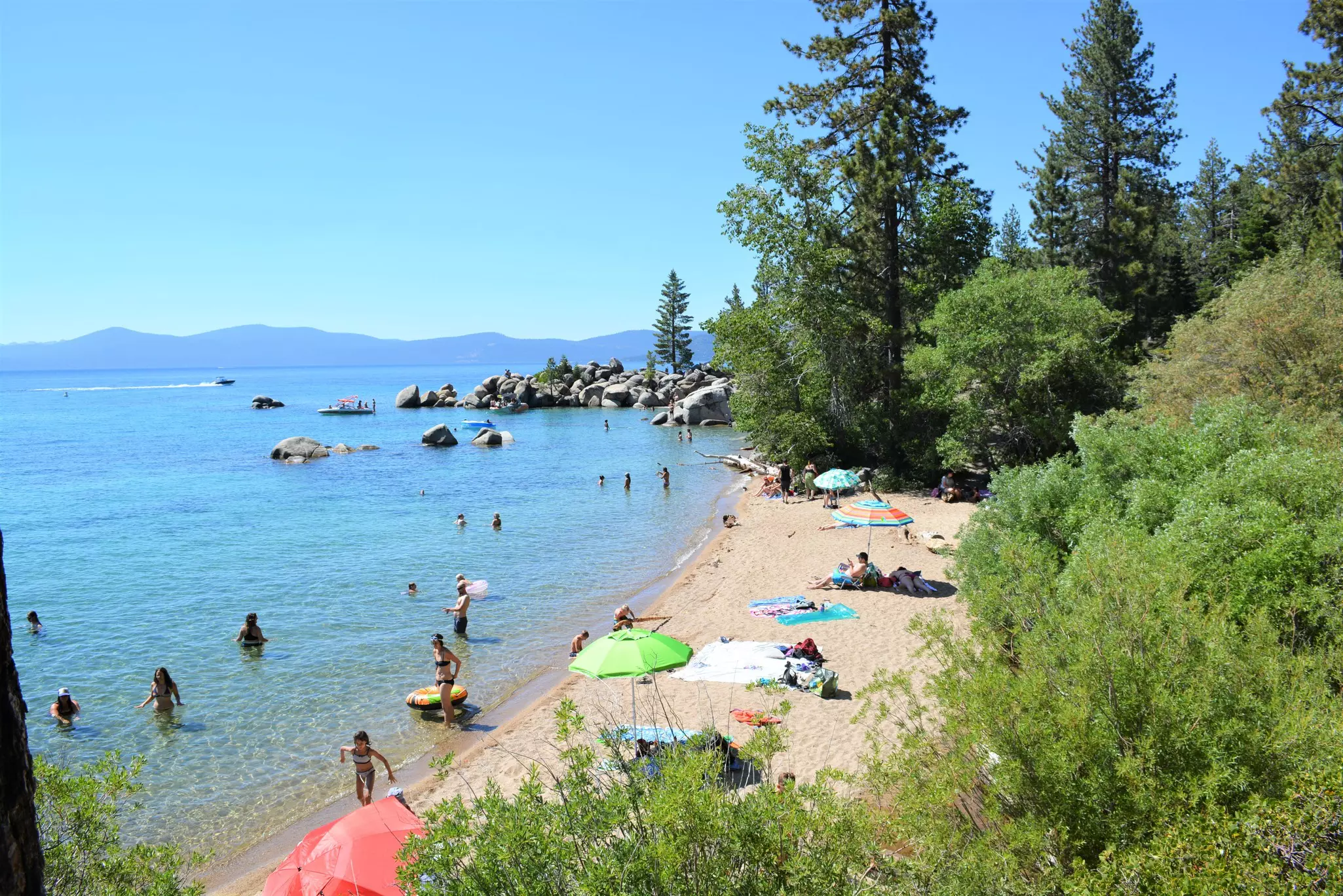 A small curve of golden sand with a few colorful umbrellas. People relax on the beach or stand in the lake