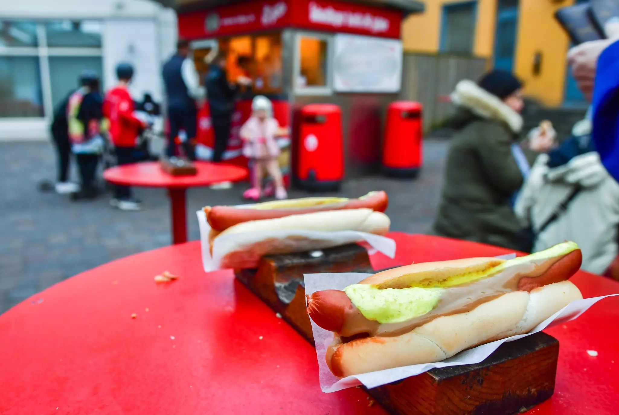 Two hot dogs topped with sauce sit on an outside table at a kiosk selling fast food snacks.