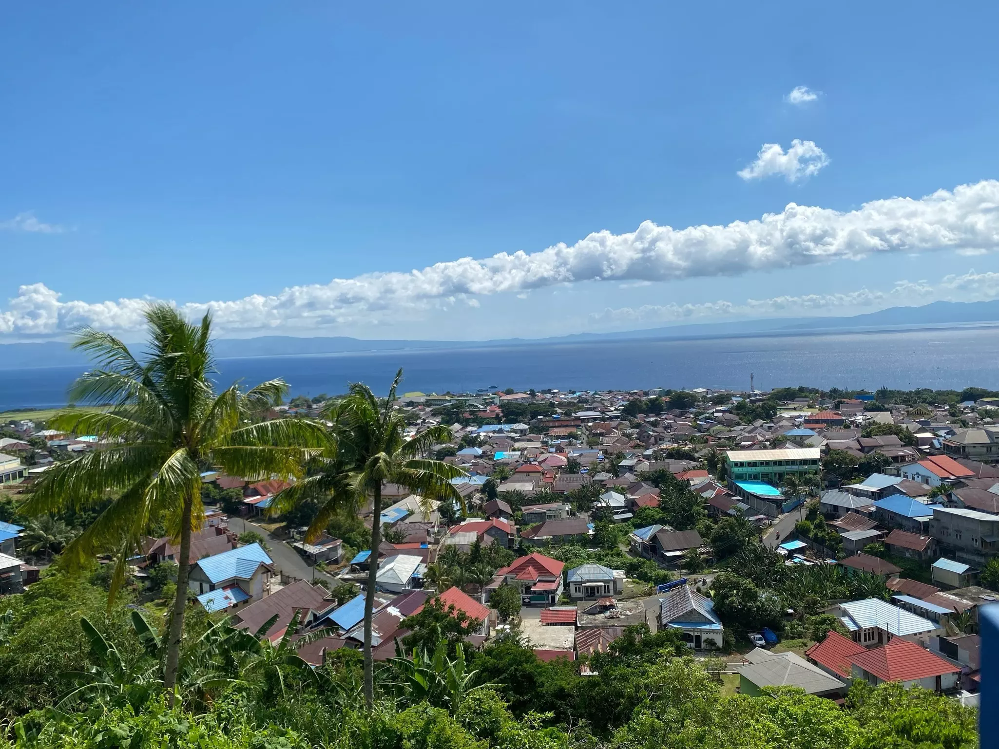 A view over a village with colorful roofs towards the sea and an island in the distance.