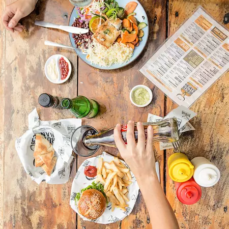 Two people sit at a wooden table eating a salad and a burger with fries. 