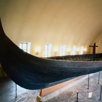A clinker-built Viking longship on a cradle beneath a white barrel-vaulted ceiling