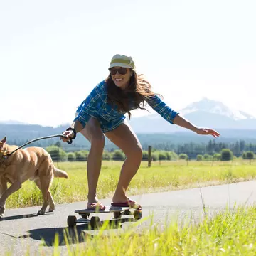 A woman skateboarding with her dog pulling her and a big mountain visible behind them