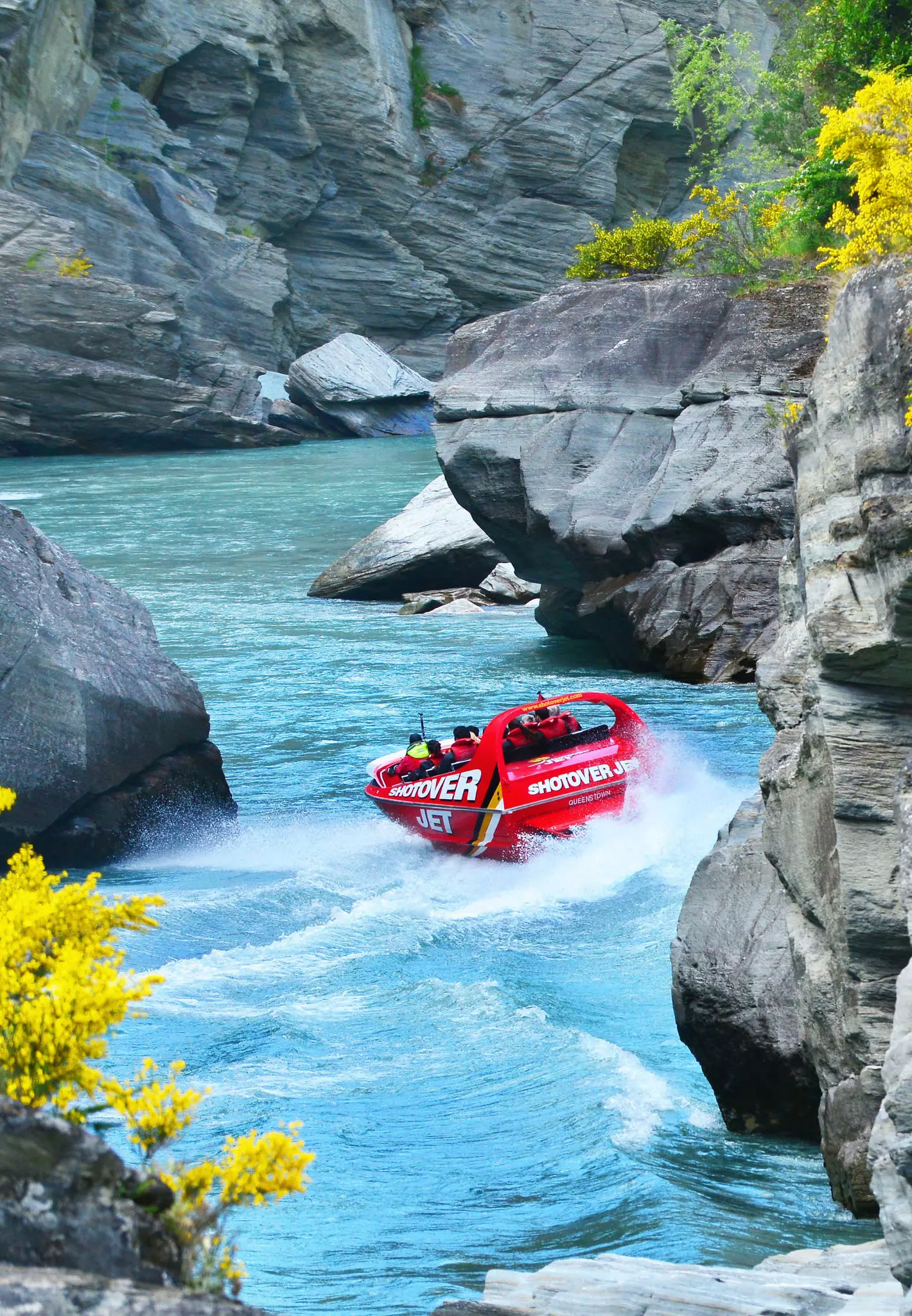A red speed boat shoots down a river with steep canyon walls either side