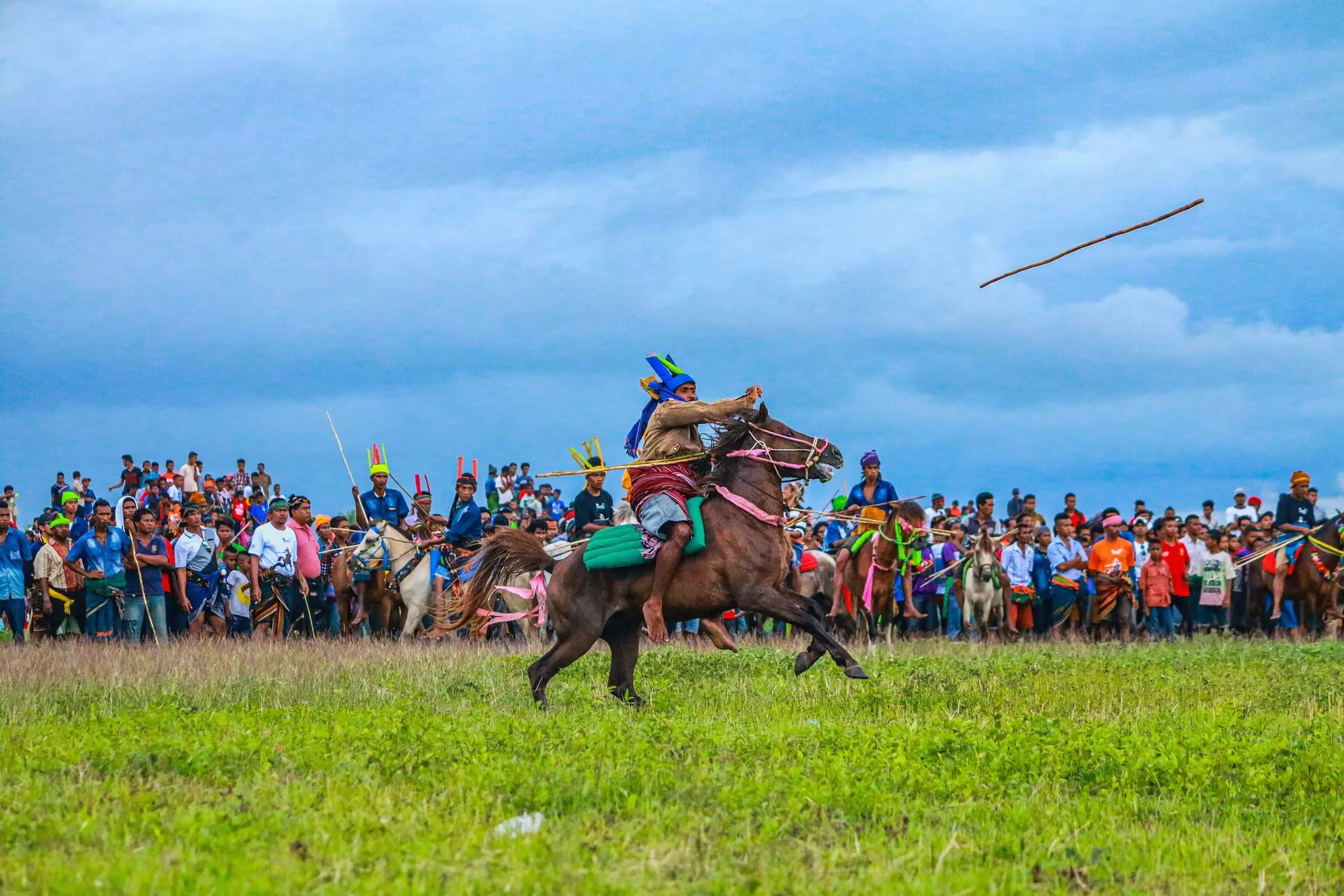 A horseback rider throws a wooden spear during a festival with many onlookers.