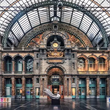 The interior of a grand station with a clock, glass ceiling and ornate windows